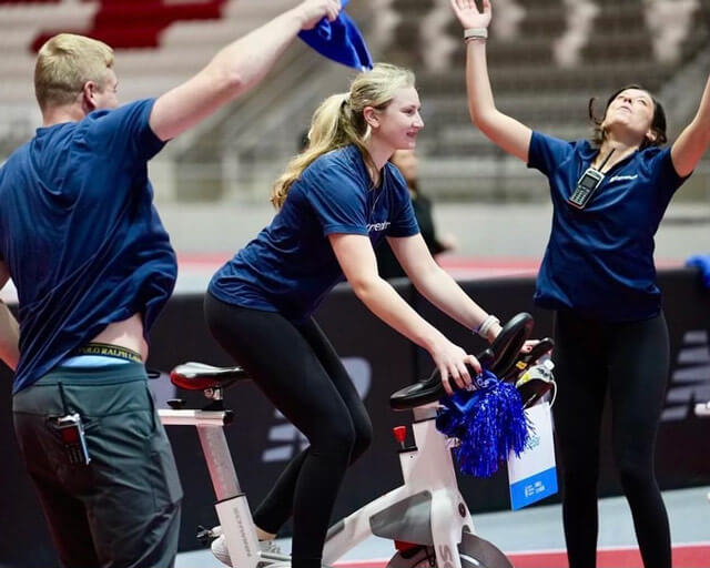 Katie on the stationary bike, banked by her cheerleaders